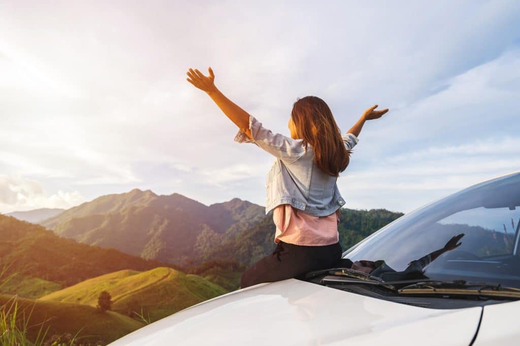Frau sitzt auf Auto und sieht über die Berge